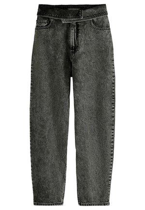 Femme portant une veste en jean noire délavée courte et un jean taille haute assorti avec un gilet en maille blanc à motifs et des bottines marron.