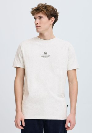 Ljusbeige t-shirt tillverkad av mjukt material, med rund halsringning och korta ärmar. Framsidan har en svart logotyp med en krondesign.