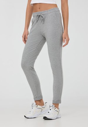 Szare spodnie dresowe wykonane z miękkiego materiału, z elastycznym paskiem na sznurki i tapered nogawkami. Noszone z białymi sportowymi sneakerami.