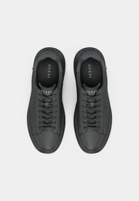 Paire de baskets en cuir Guess noires avec lacets et semelles intérieures de marque, vues de dessus sur un fond clair uni.