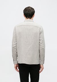 Svetlosivé ľanové tričko s rovnakým strihom, zapínanými manžetami a detailom vzadu na chrbte, v kombinácii s čiernymi nohavicami.