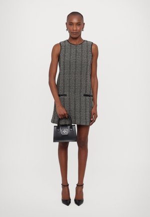 Abito tweed in bianco e nero con maniche corte, strisce verticali e due tasche; abbinato a una piccola borsa nera e tacchi neri a punta.