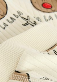 Tkanina pikowana w kolorze kremowym z żebrowaną teksturą. Widoczne są nadruki twarzy kreskówkowego renifera oraz tekst, co dodaje zabawnego charakteru.