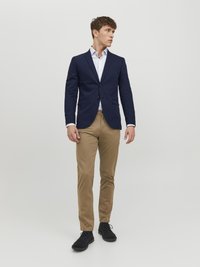Blazer navy avec fermeture à un bouton, chemise blanche à boutons, pantalon khaki et chaussures noires. Design ajusté avec deux poches avant.