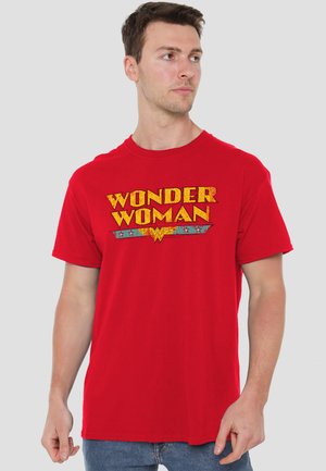 Man wearing red Wonder Woman T-shirt looking to his right against plain gray background.