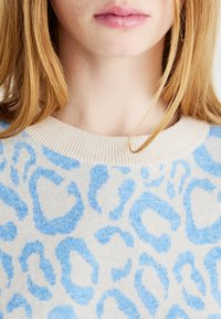 Μπλε λεοπάρ παλτό με κρεμ φόντο, ριμπ τριγωνικό λαιμό και απαλό ύφασμα. Επικέντρωση στο σχεδιασμένο ύφασμα και την αντίθεση χρωμάτων.