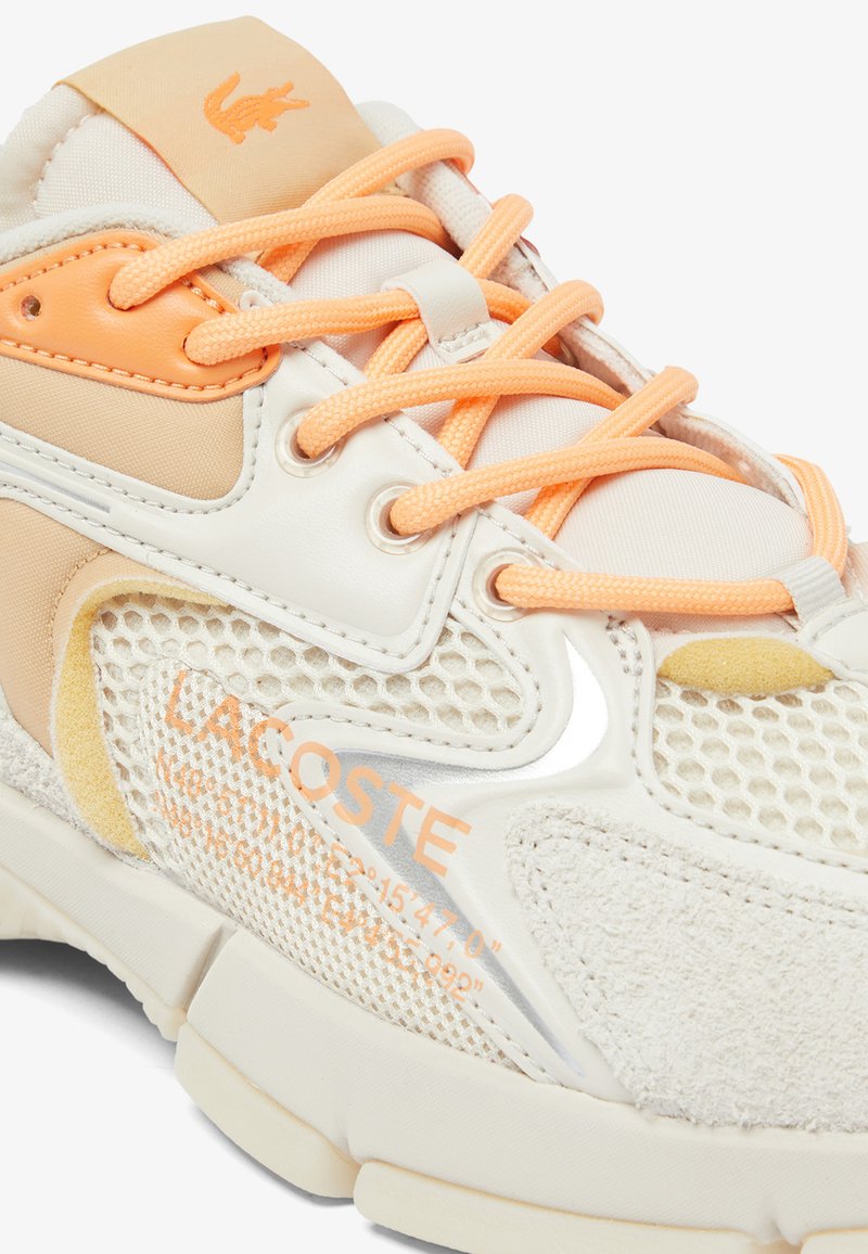 Zapatillas Lacoste con parte superior de malla beige, acentos naranjas, cuero texturizado y suela blanca. Presentan el logo y costuras con patrón.