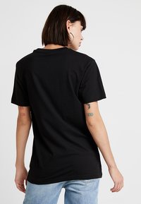 Sort bomulds t-shirt med rund hals og korte ærmer. Synlige syninger. Modellen har lyseblå jeans på, som viser en afslappet pasform.