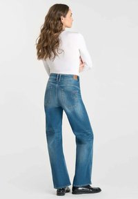 Jeans in denim azzurro chiaro con forma a campana, dotati di tasche posteriori e un'etichetta in pelle marrone sulla vita. Texture liscia.