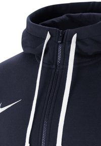 Navy zip-up hoodie with a high collar, white drawstrings, and a white Nike logo on the left chest. Soft texture, casual design.