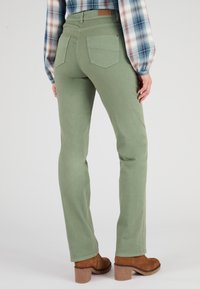Pantaloni verdi a gamba dritta con tasche posteriori, realizzati in tessuto liscio. Abbinati a stivaletti marroni con tacco e una camicia a quadri.