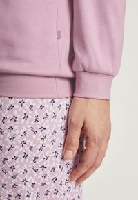 Felpa rosa chiaro con polsini delle maniche arricciati, abbinata a un tessuto rosa con un piccolo motivo floreale bianco e navy.