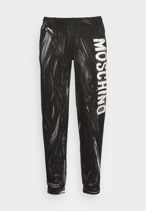 Mustat collegehousut, joissa kiiltävä, abstrakti valkoinen maalauksellinen kuvio ja sivussa näkyvä valkoinen "MOSCHINO"-logo. Kuminauhavyötärö.