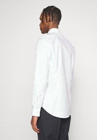 Chemise blanche à boutons avec un col classique, des manches longues et un ourlet arrondi ; fabriqu�ée en tissu coton lisse ; dispose de boutons aux poignets.