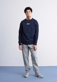 Sudadera azul marino con un logo en el frontal, combinada con pantalones de chándal gris claro. El conjunto presenta un diseño casual y telas texturizadas y cómodas.
