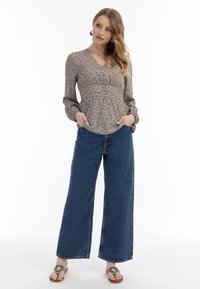 Långärmad blus med v-ringning och blommönster i dämpade färger, i kombination med vida mörkblå jeansbyxor och platta sandaler.