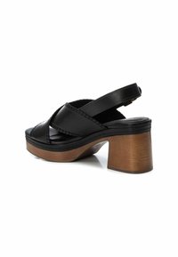 Zwarte leren sandaal met een kruisbandontwerp, een gevoerd voetbed en een stevig houten blokhak. De gestructureerde afwerking op de hak zorgt voor grip.