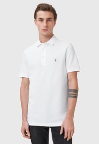 Polo bianco in cotone, con colletto classico, patta con tre bottoni e un piccolo logo nero sul lato sinistro del petto.