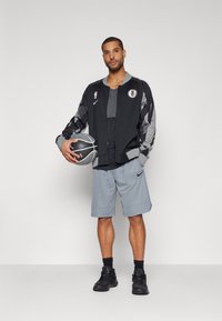 Black and gray athletic jacket with NBA logo, gray t-shirt, gray basketball shorts, and black sneakers. Holding a basketball.