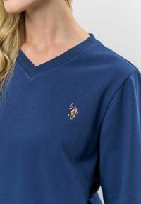 Tumši zils v veida kakla t-krekls, izgatavots no kokvilnas maisījuma, ar nelielu izšutu logotipu uz kreisā krūšu. Mīksta tekstūra ar īsām piedurknēm.