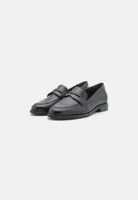 Mocasines de cuero negro con un acabado suave, que presentan una correa decorativa y un tacón bajo y resistente para un uso cómodo.