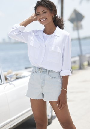 White button-up shirt with two chest pockets, paired with light blue denim shorts. Textured fabric, rolled sleeves, and a light belt accent.
