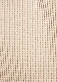 Beige knitted fabric with vertical ribbing texture, featuring fine stitching and slight variations in tone throughout. Soft and stretchy material.