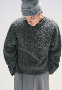 Hustá, textúrovaná tmavosivá sveter s voľným strihom a okrúhlym výstrihom, kombinovaná s rebrovanou sivou čiapkou a strihanými sivými nohavicami.