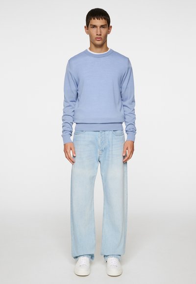 Light blue sweater featuring a round neck, ribbed cuffs, paired with faded light blue wide-leg jeans and white sneakers.