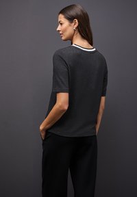 Top negro de manga corta con un acabado texturizado, borde blanco en el cuello y corte relajado, combinado con pantalones negros.