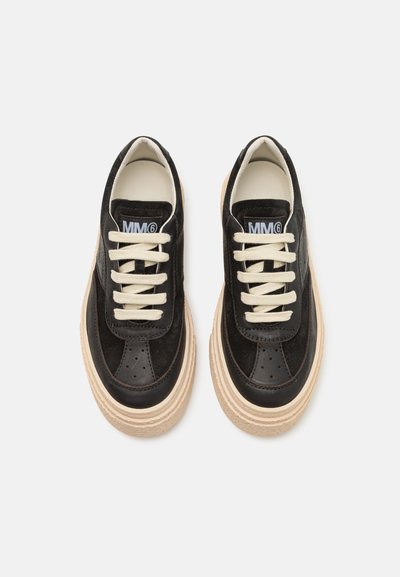 Svarta mocka sneakers med krämfärgade snören, med perforerade detaljer och en tjock beige sula. Logotyp synlig på tungan.