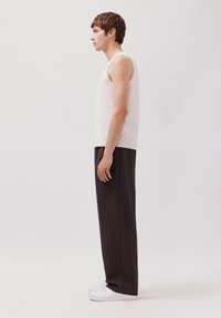Weißes Tanktop, schwarze weit geschnittene Hose und weiße Sneaker, seitlich dargestellt. Das Tanktop besteht aus leichtem Stoff und hat ein enganliegendes Design.