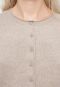 Beige knitted cardigan with a round neckline, featuring six matching buttons along the front and a soft texture.
