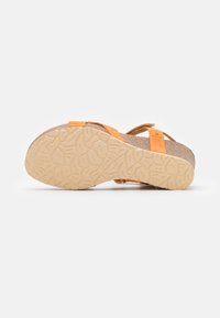 Sandale avec semelle beige texturée, semelle intérieure en liège et lanières en cuir orange, vue de dessous sur un fond uni.