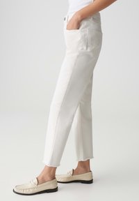 Jeans rectos blancos de denim, con dobladillo deshilachado y bolsillos laterales, combinados con mocasines beige sin hebillas.