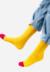 Żółte skarpetki z czerwonymi akcentami na palcach, gładka faktura, długość do połowy łydki, zestawione z podwiniętymi dżinsami.