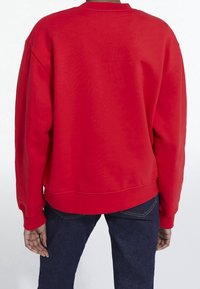 Sudadera de cuello redondo roja, confeccionada con tela suave y con un ajuste holgado. Costuras favorecedoras y puños acanalados, sin marcas ni patrones visibles.