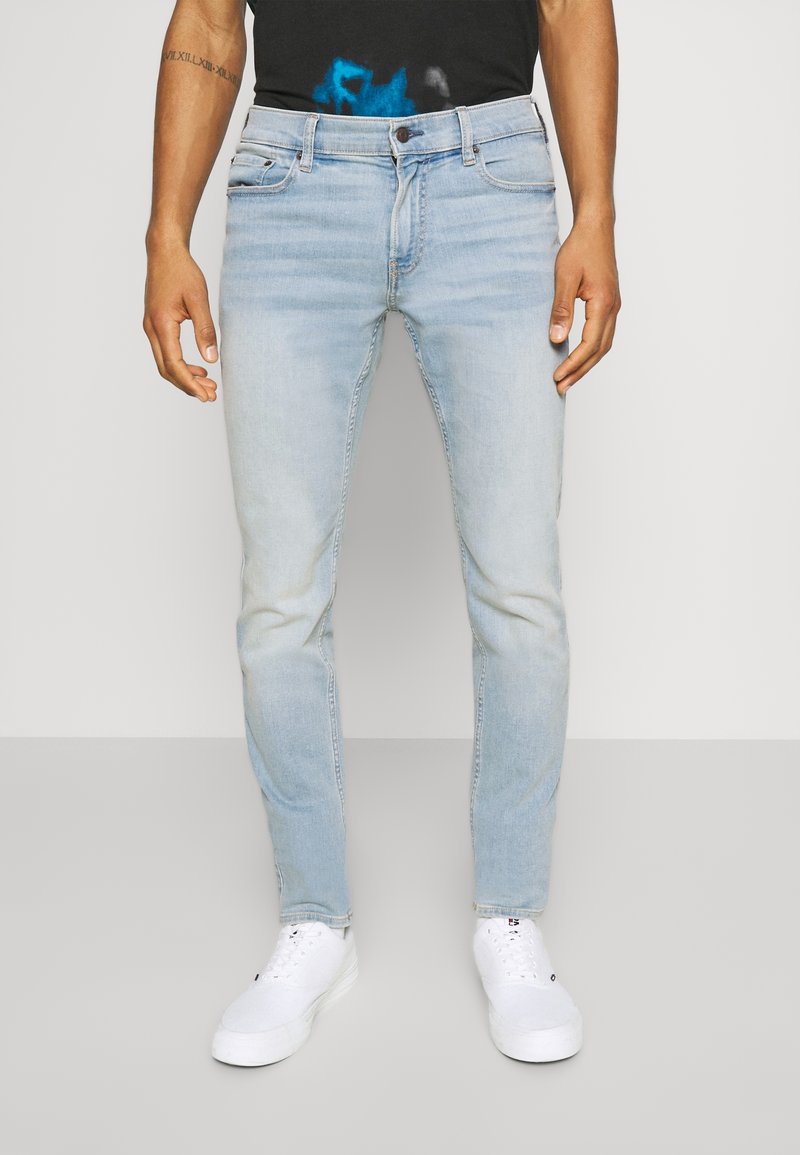 Ljusblå denimjeans med slim fit-design, som har fem fickor och ljusa slitningar för en avslappnad look, kombinerade med vita sneakers.