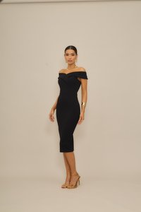 Μαύρο, μίντι φόρεμα με έξω τους ώμους, σφιχτή γραμμή και διακριτικές πιέτες. Φοριέται με χρυσά αξεσουάρ και μπεζ πέδιλα με λωρίδες.