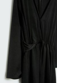 Černé dlouhé šaty s texturovanou tkaninou, s překříženým designem a nařaseným pasem. Elegantní silueta a měkké záhyby.