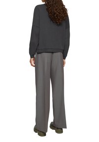 Szara bluza z luźnym krojem i długimi rękawami, zestawiona z szerokimi szarymi spodniami i masywnymi oliwkowymi butami. Teksturowana tkanina.