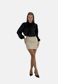 Blusa nera di raso con maniche a sbuffo, abbinata a una gonna attillata beige con bottoni decorativi, indossata con décolleté nere a punta.