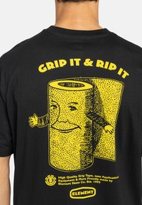 Black t-shirt featuring yellow graphic of a smiling roll with arms, text "GRIP IT & RIP IT," and brand logo. Soft cotton material.