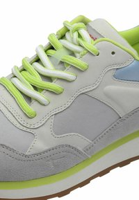 Grijze en witte sneaker met een gestructureerde bovenkant, limoen groene veters en accenten, en een lichtblauw paneel; heeft een dikke zool en zichtbare stiksels.