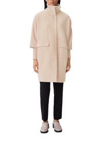 Vaaleanpunainen villasekoitetakki, jossa korkea kaulus, kaksi etutaskua ja resorit hihansuissa. Yhdistetty mustiin housuihin ja beigen sävyisiin loafer-kenkiin.