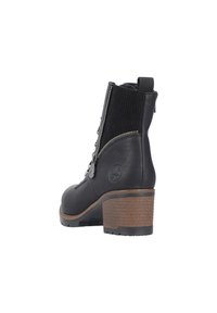Bottine noire avec un extérieur en cuir, panneau élastique texturé, et un talon en bois moyen. Présente une fermeture éclair sur le côté et un détail de logo sur le talon.