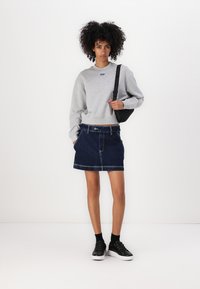 Gray sweatshirt with a small blue logo, paired with a dark denim skirt, black sneakers, and a black shoulder bag. White background.
