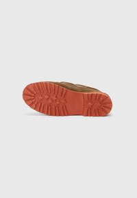 Brun mockaskinnsko med en texturerad orangegummisula som har djupa mönster och ett logotryck för grepp och hållbarhet.