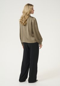 Blusa in satin verde oliva con maniche a sbuffo e polsini con bottoni, abbinata a pantaloni neri larghi, caratterizzati da una vestibilità comoda e una texture liscia.