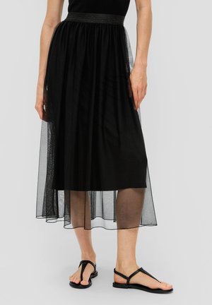 Jupe noire midi avec une superposition en tulle transparent en couches, une doublure unie et une taille élastiquée. Associée à des sandales plates noires.